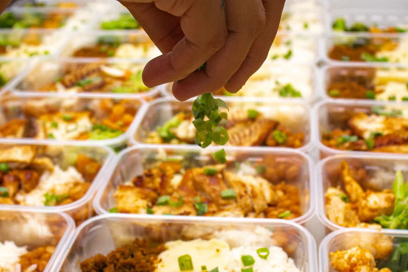 Hands finishing a row of prepped meals.